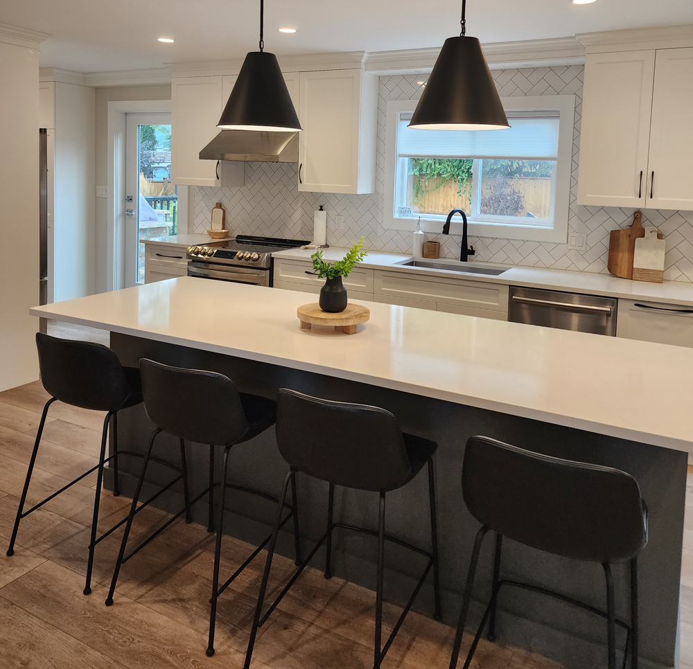 coquitlam-2 A modern kitchen featuring white cabinets and sleek black stools arranged around a central island.